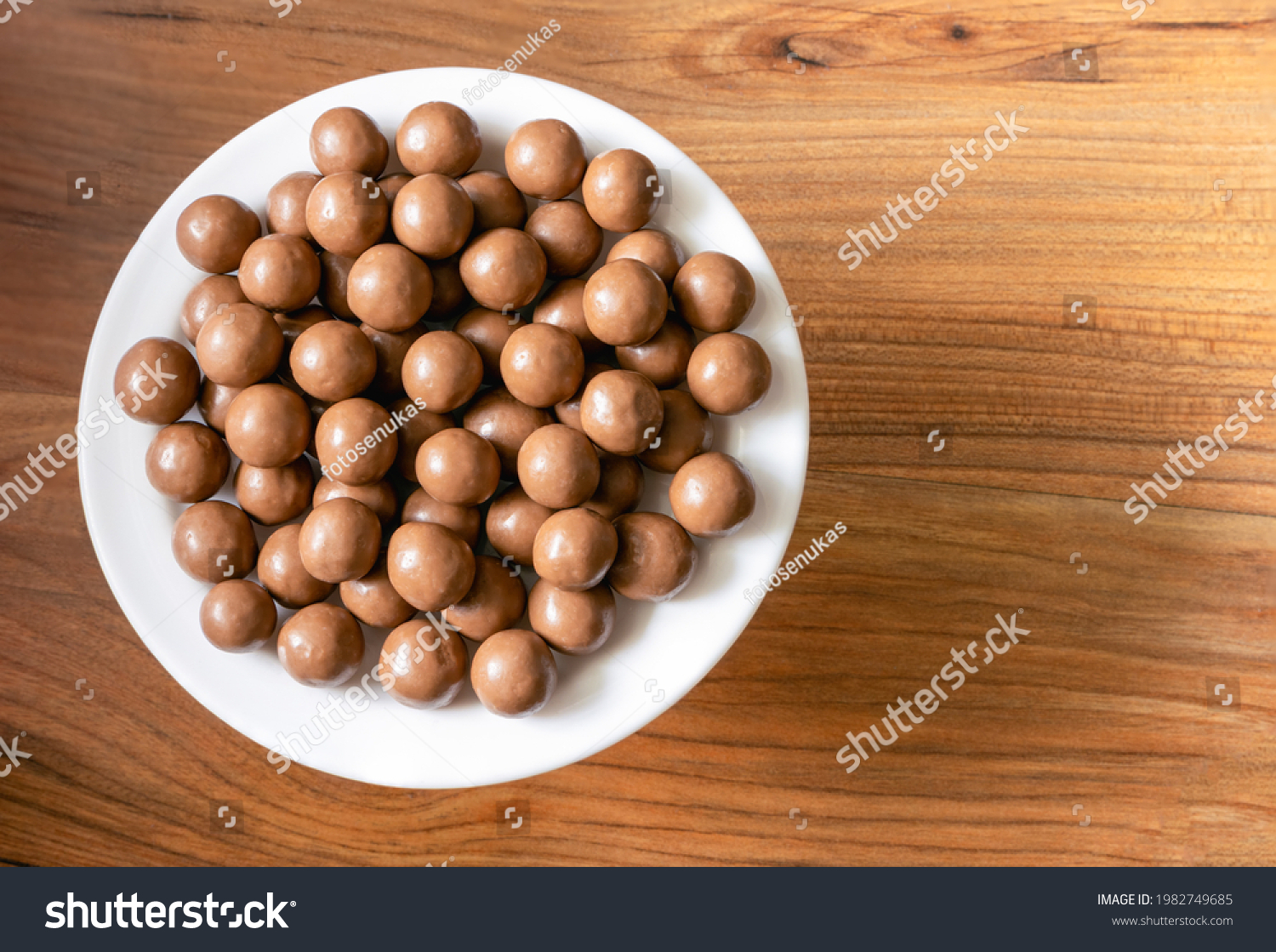 Maltesers milk chocolate balls on a plate on a pine tree surface, top view #1982749685