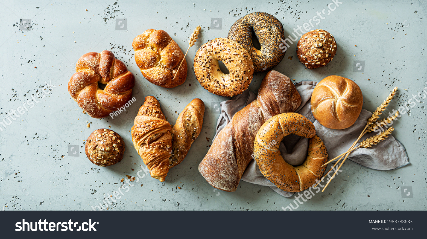 Bakery - various kinds of breadstuff. Bread rolls, bagel, sweet bun and croissant captured from above (top view, flat lay). Grey stone background. #1983788633