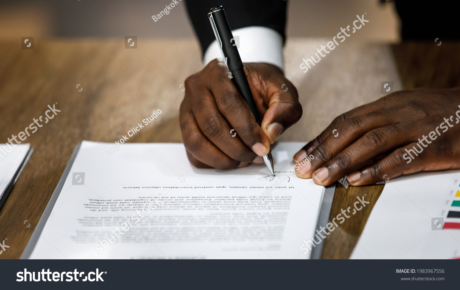 Close up and selective focus on African black formal professional business male hands holding pen, signing in white paper form or application to confirm and deal contract agreement on table #1983967556