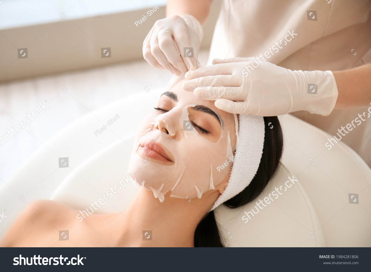 Cosmetologist applying sheet mask on woman's face in beauty salon #1984281806