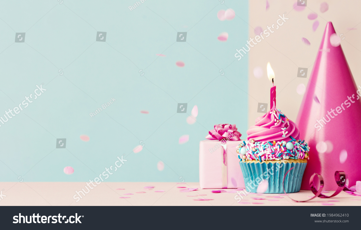 Birthday background with pink birthday cupcake and candle, birthday gift and party hat #1984962410