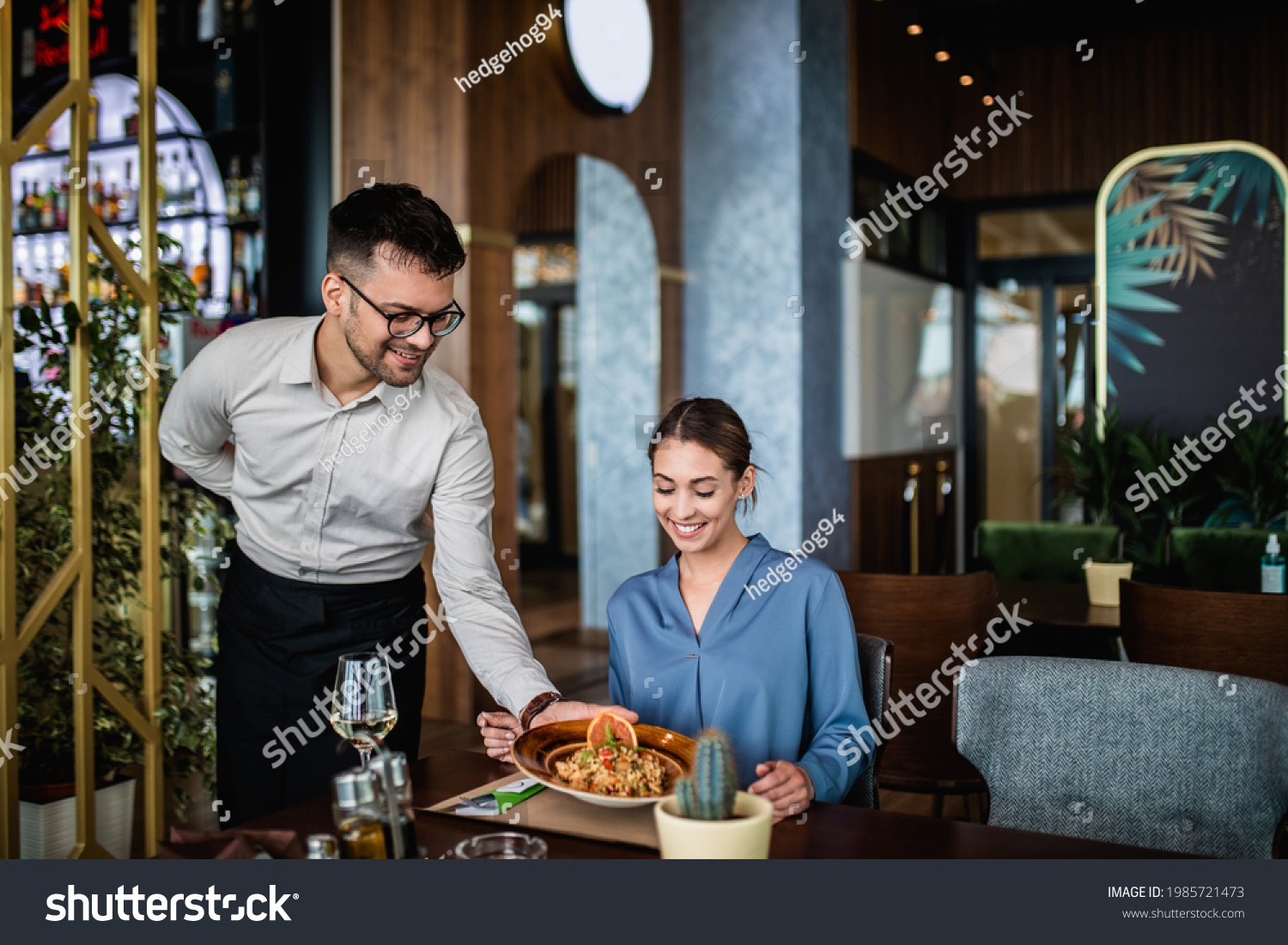 Young waiter with face protective mask serving delicious meal to beautiful woman in restaurant.  #1985721473