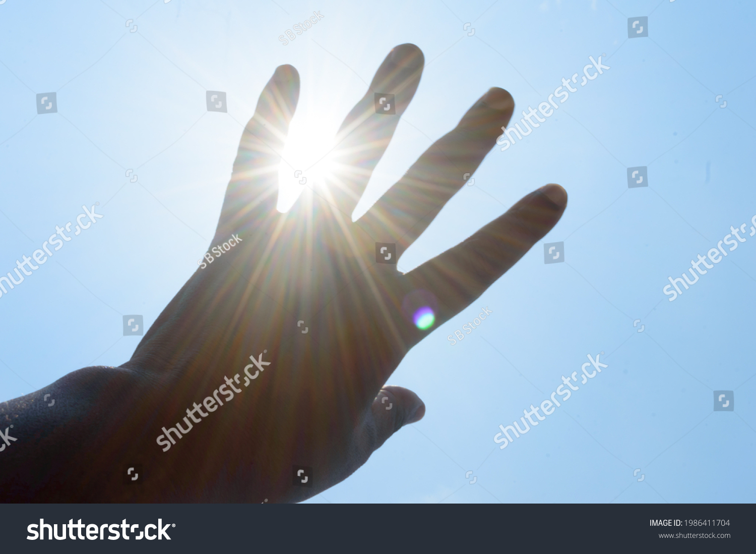 Hot summer sunlight rays pouring through human hand. Hand covering sun light heat temperature.  #1986411704