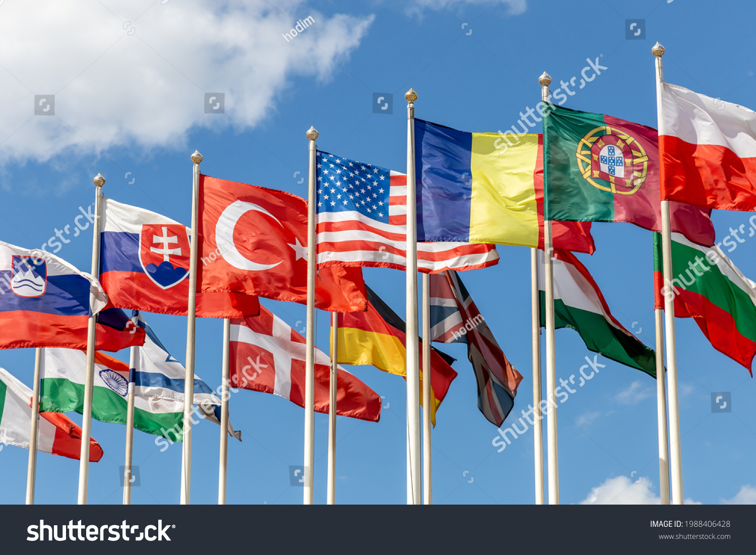 Group of flags of various states - as a symbol of world cooperation. Flags of the countries of the world on flagpoles flutter in the wind against the background of a blue sky #1988406428