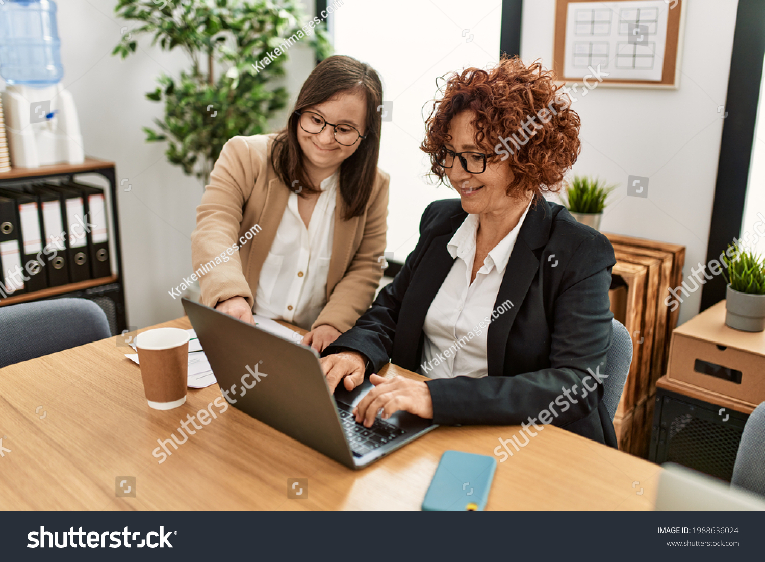 Group of two women working at the office. Mature woman and down syndrome girl working at inclusive teamwork. #1988636024