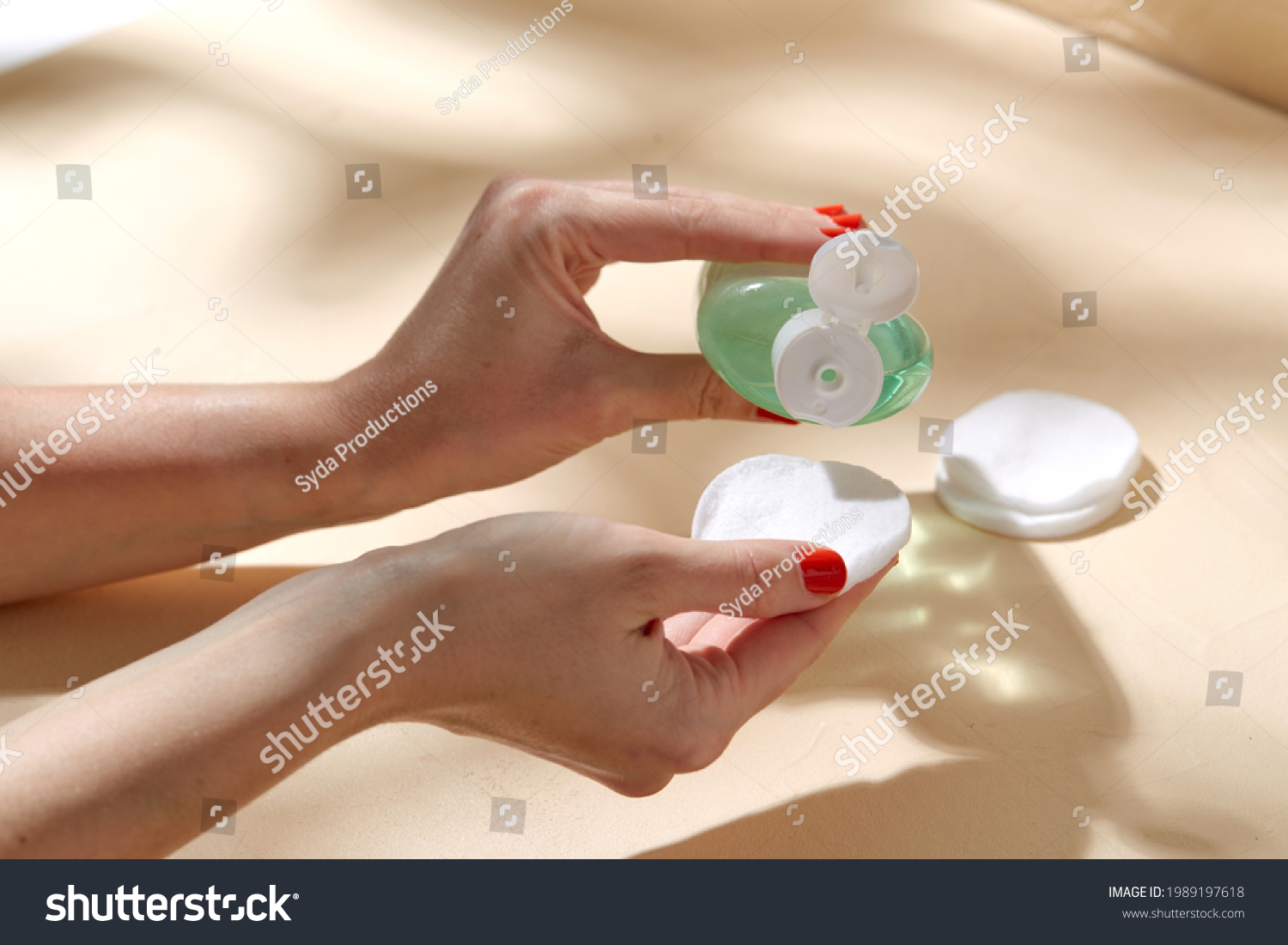 beauty, cosmetics and skincare concept - close up of hands applying lotion to cotton pad over beige background with shadows #1989197618