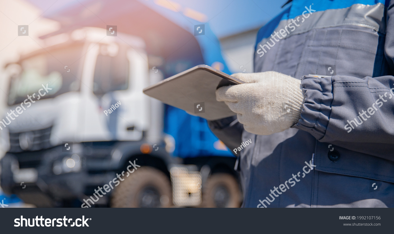 Concept banner automated logistics online internet. Dump truck driver man in uniform with tablet computer controls loading of cargo or coal. #1992107156