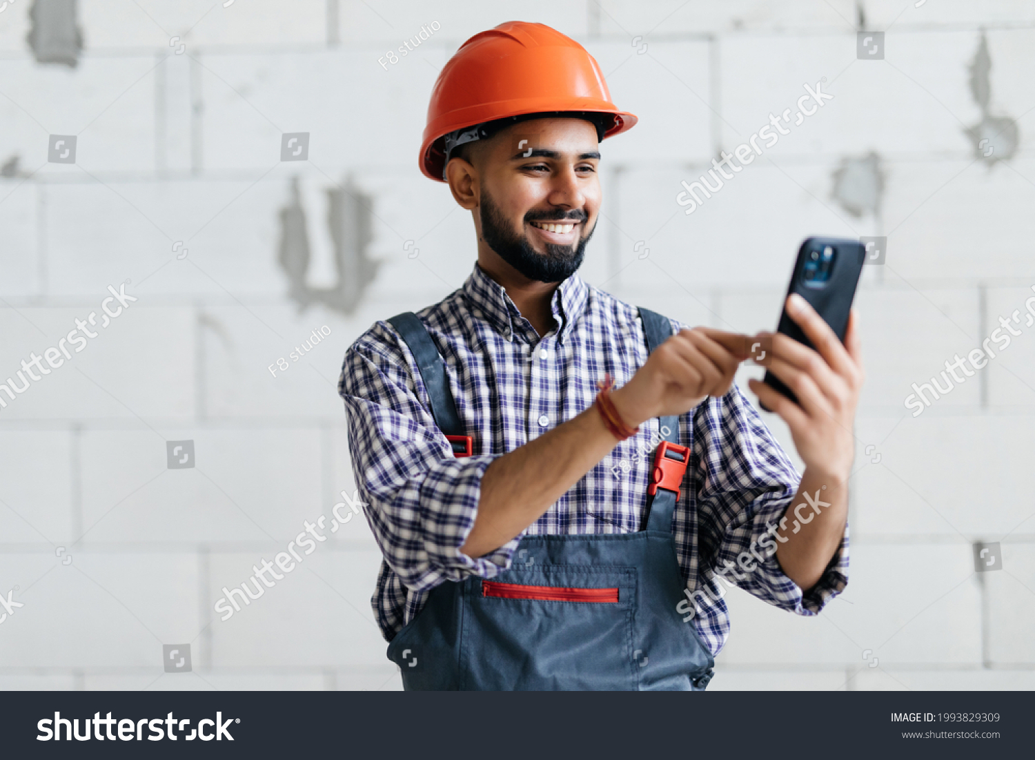 Indian builder checking a message on his mobile phone or making a call in a new build house #1993829309
