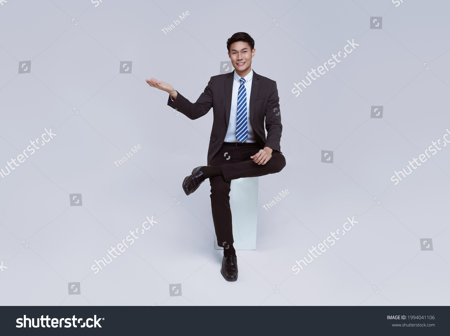 Handsome and friendly face asian businessman smile in formal suit sitting on chair points his hands to presented on white background studio shot. #1994041106