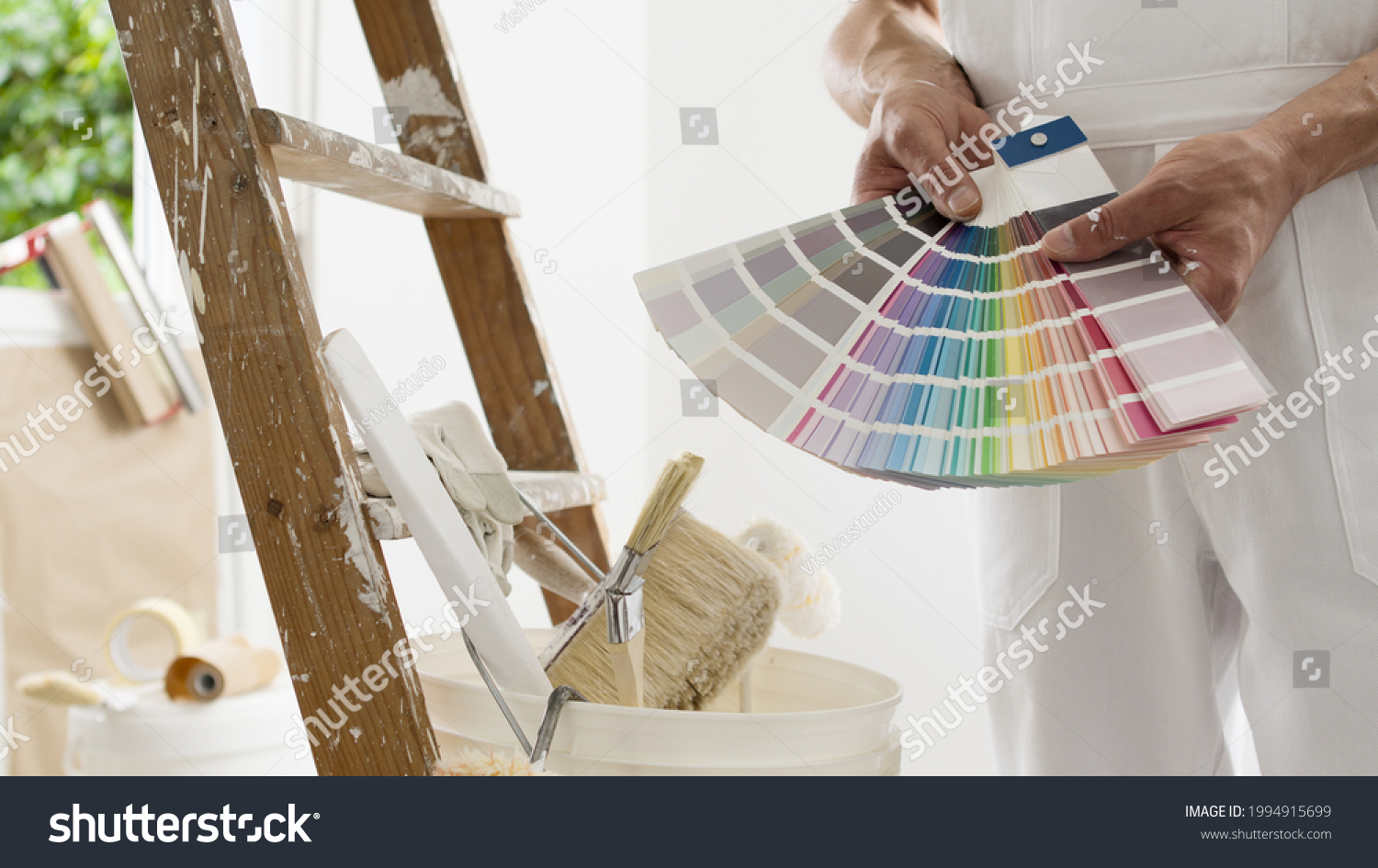 hands of house painter man decorator choose the color using the sample swatch, work of the house to renovate, a wooden ladder with paint brushes and a bucket as a background, close up #1994915699