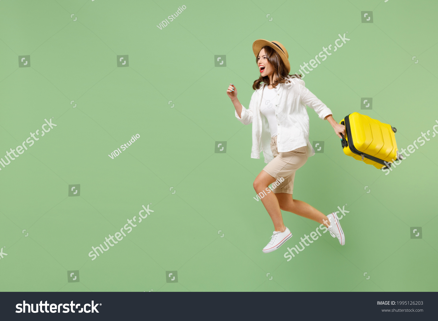 Full length traveler tourist woman in casual clothes straw hat jump high hold suitcase run isolated on pastel green background. Passenger travel abroad on weekends getaway. Air flight journey concept #1995126203