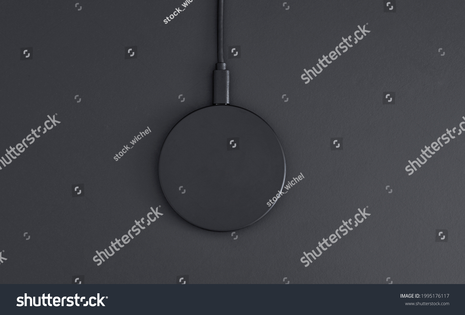 High angle view of black plastic circular wireless charger laying on dark grey desk. Modern technology, wireless device and transfer of energy concept. #1995176117