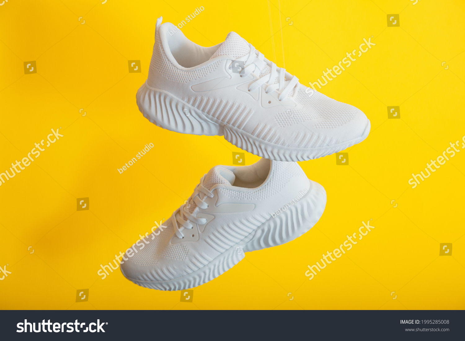 White sneakers shoes fly on yellow color background. Pair of sport male sneakers. Levitation footwear on yellow wall #1995285008
