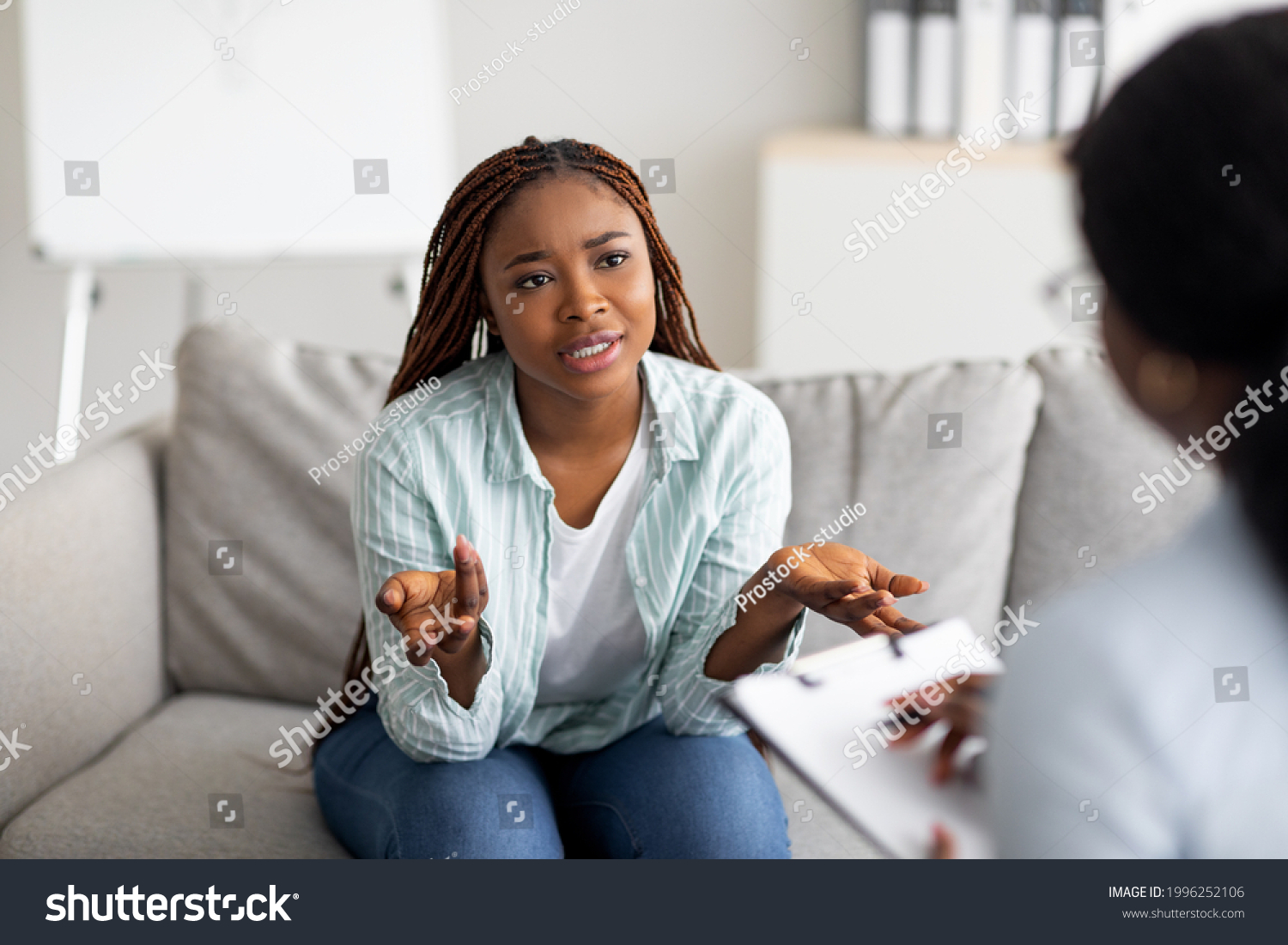 Mental health and psychological assistance concept. Young worried black woman having counseling session with psychotherapist at clinic. PTSD disorder, anxiety treatment #1996252106