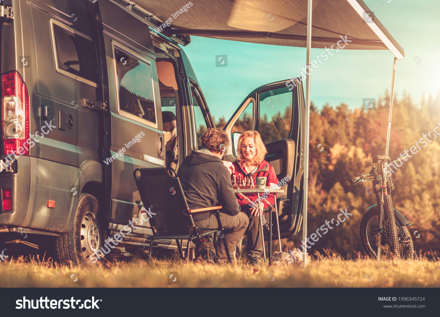 Caucasian Couple Playing Chess Next to Their Camper Van RV During Vacation Camping Time. Recreational Vehicles and Road Trip Theme. #1996345724