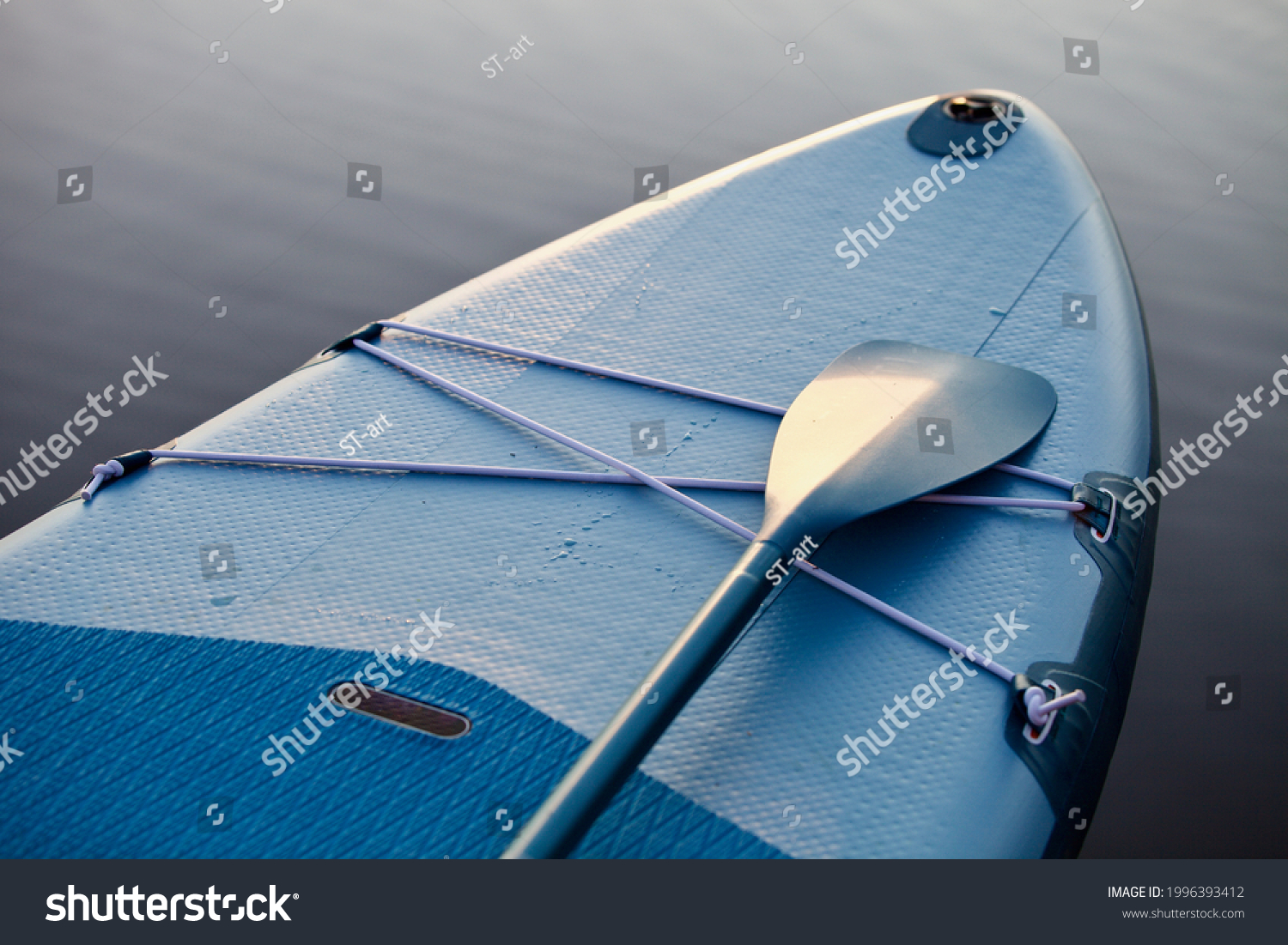 Paddle board and surf board with paddle on blue water surface background close up. Surfing and SUP boarding equipment in sunset lights close-up. Outdoor water sports. Surfing lifestyle backgrounds. #1996393412