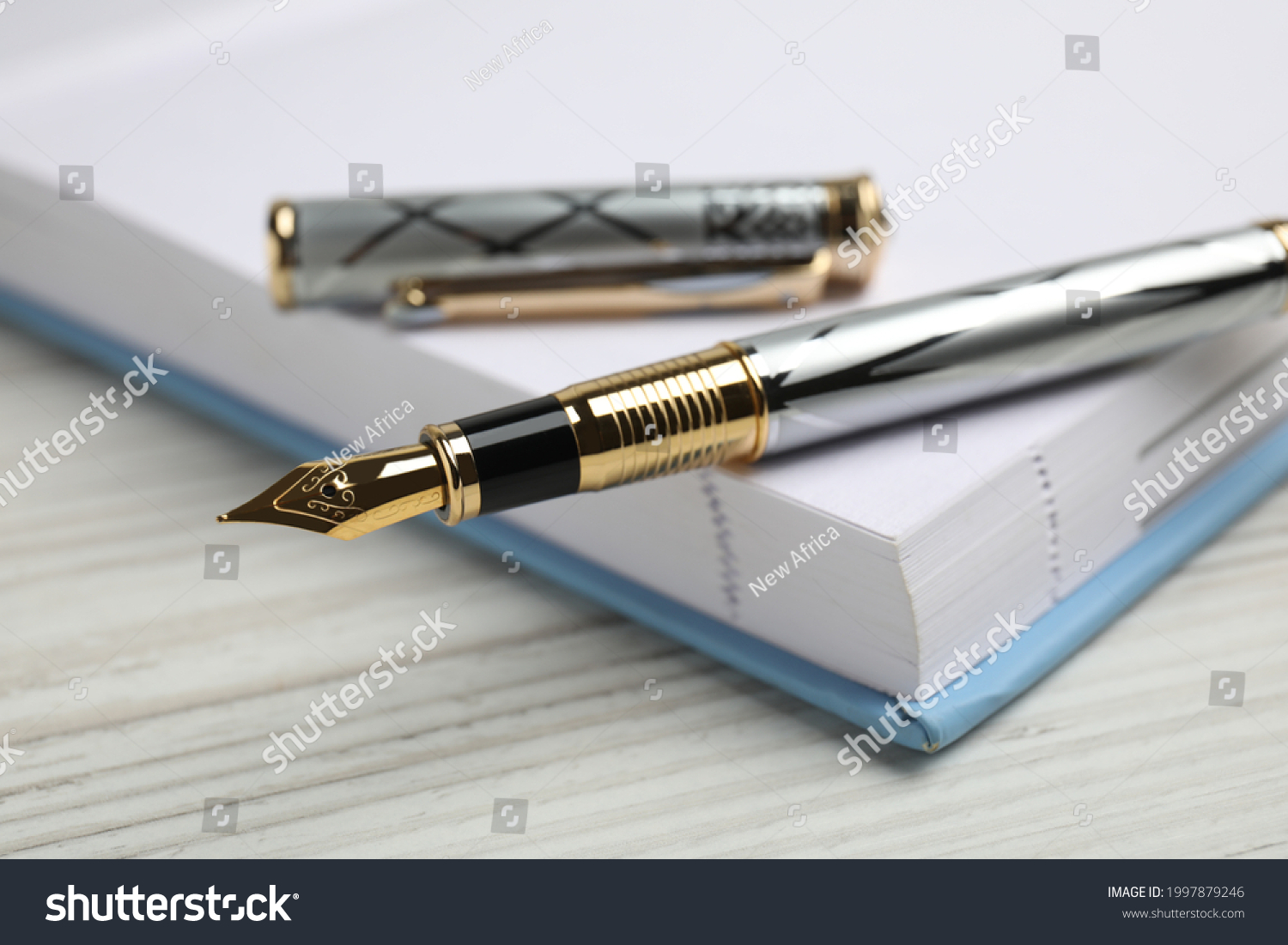Beautiful fountain pen with ornate nib and notebook on white wooden table, closeup #1997879246