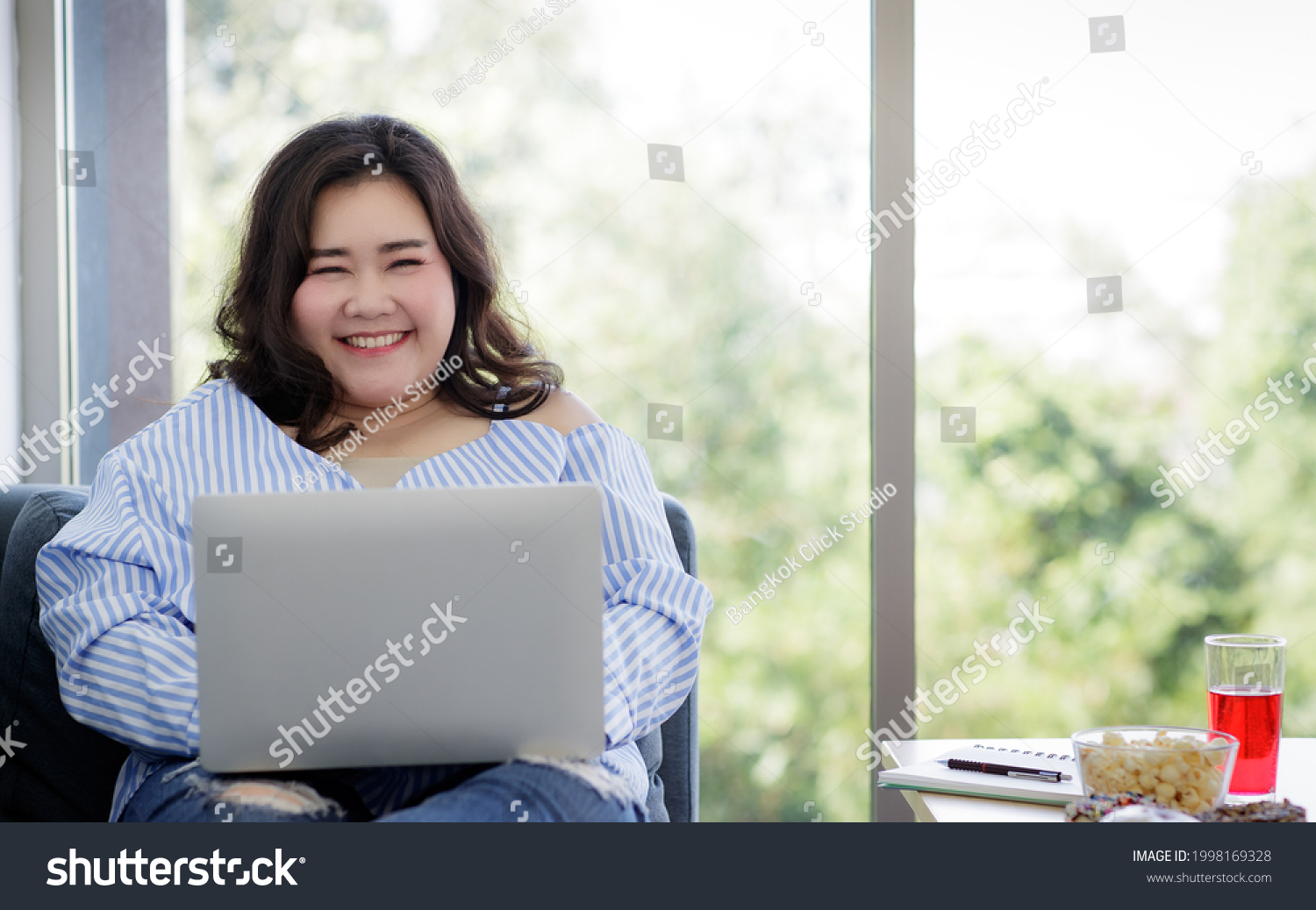 Asian young happy beautiful female model sit relaxing on sofa smiling look at camera using laptop computer work from home in quarantine time from covid pandemic moment. #1998169328
