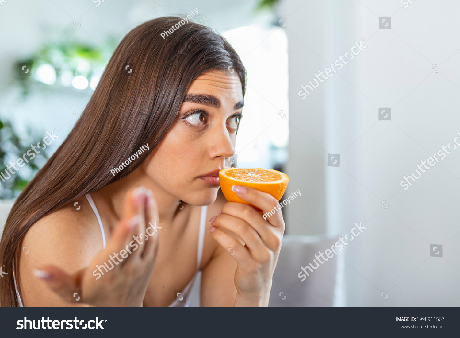 Sick woman trying to sense smell of half fresh orange, has symptoms of Covid-19, corona virus infection - loss of smell and taste. One of the main signs of the disease. #1998911567