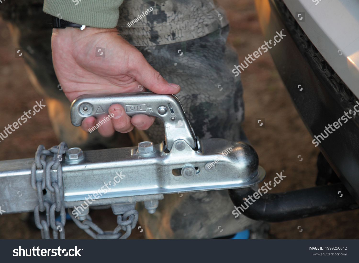 A man's hand checks the fixation of the trailer closed hitch lock handle on the towing ball towbar of the car closeup, the safety of driving with a trailer on the road #1999250642