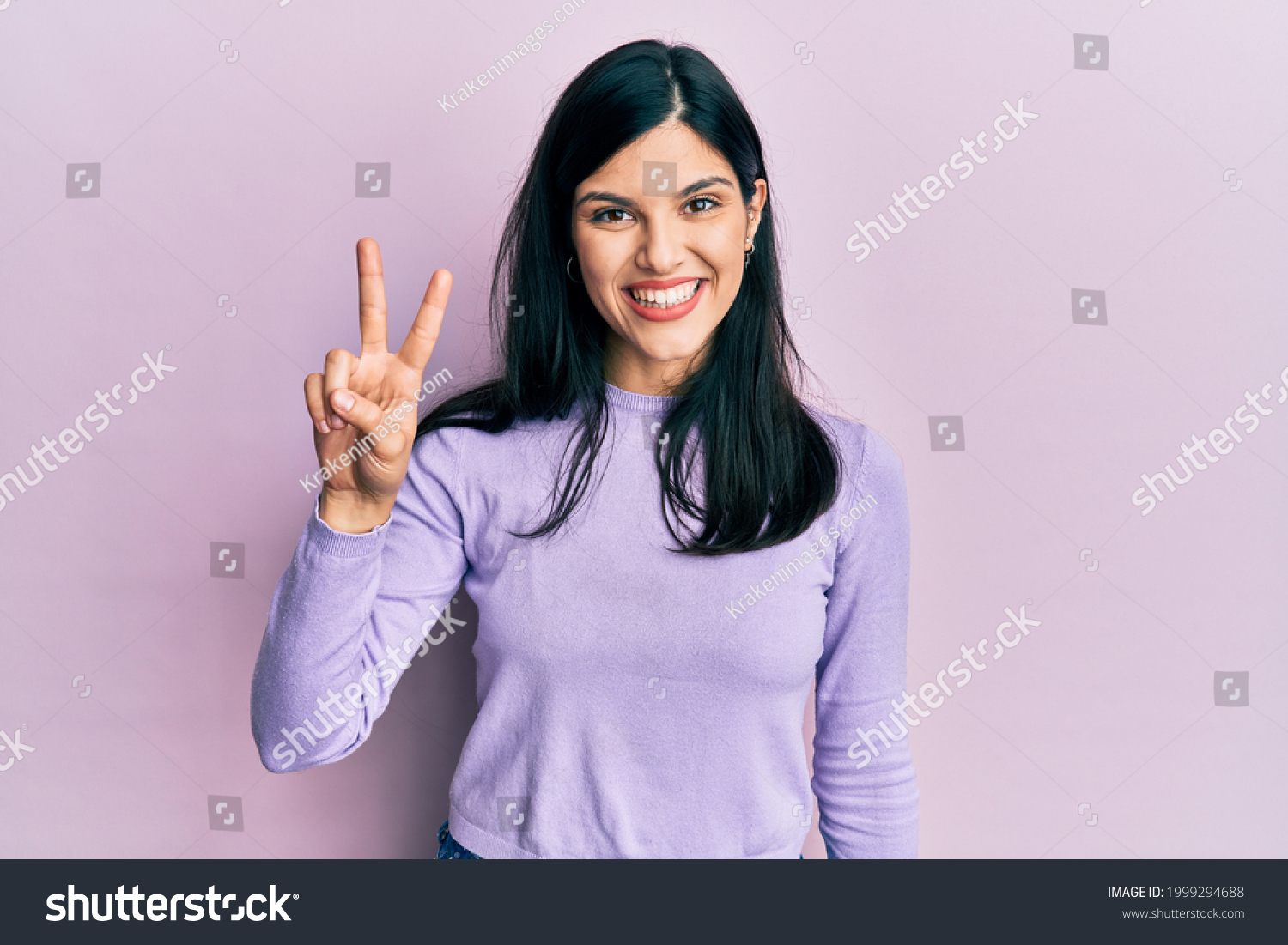 Young hispanic woman wearing casual clothes smiling looking to the camera showing fingers doing victory sign. number two.  #1999294688