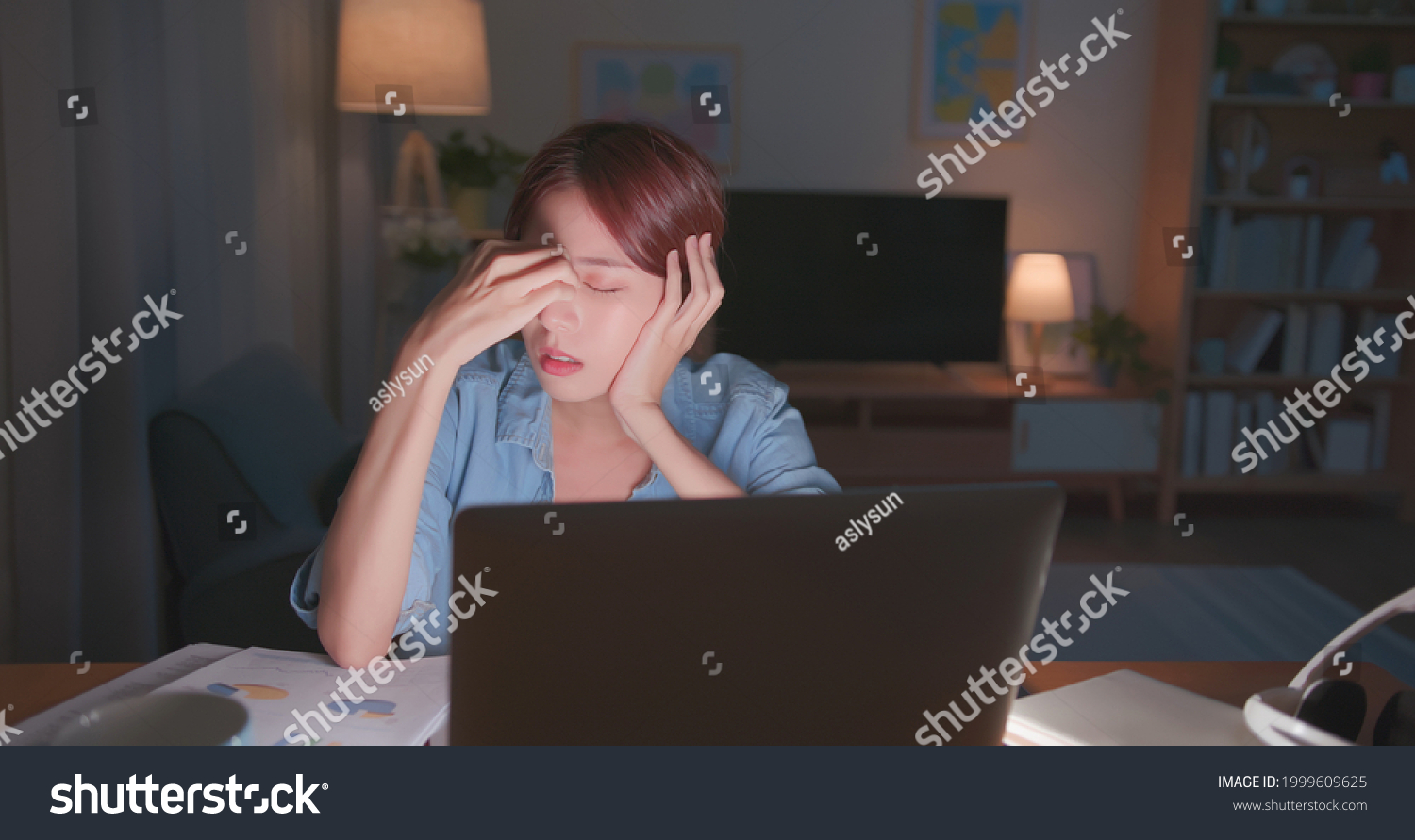 Tired young freelance worker rubbing her eyes while sitting in front of laptop computer and working on promising project - asian girl soho lady stay up late in home office eye painful #1999609625
