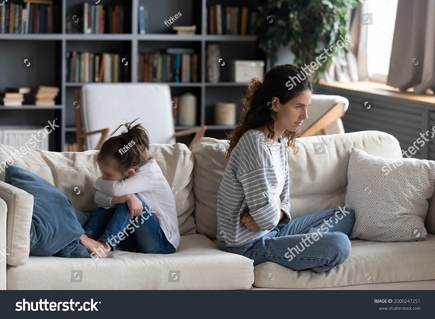 Angry Caucasian mother and small daughter sit separate back to back after family fight or quarrel. Mad unhappy mom and little kid child avoid talking, have misunderstanding. Generation gap concept. #2000247251