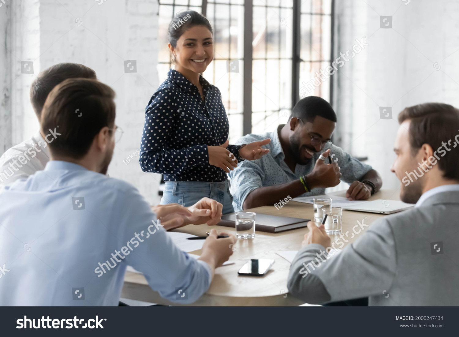 Diverse millennial business team with Indian leader discussing project, brainstorming in office, talking, laughing. Corporate teacher training staff, mentoring employees, holding meeting or training #2000247434