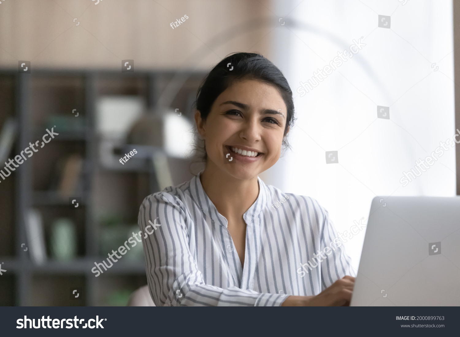 White collar. Happy young indian female accountant consultant sit at workplace by laptop take break in typing document look at camera. Headshot portrait of cheerful ethnic woman use pc in office work #2000899763