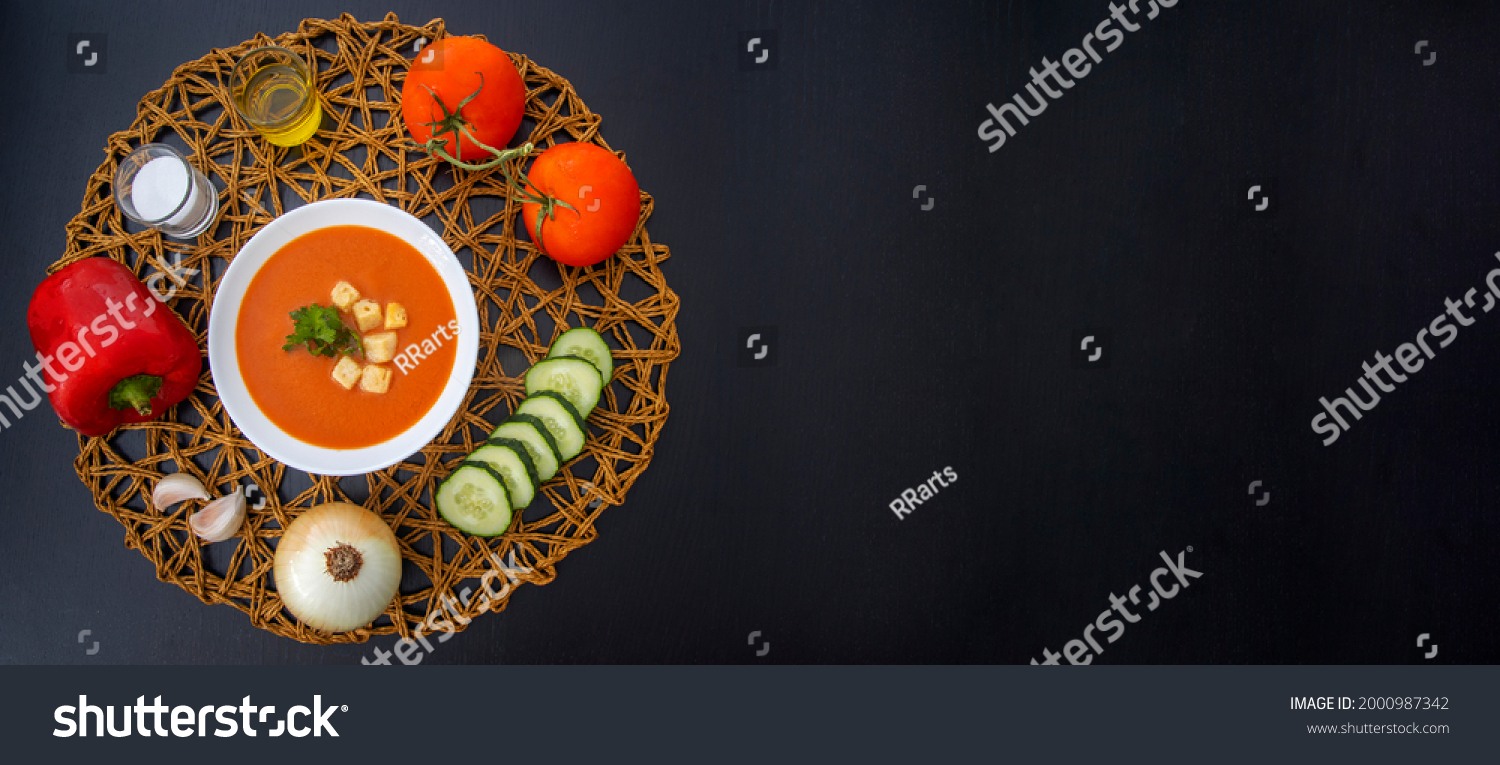 Refreshing gazpacho surrounded by its ingredients on dark wooden table #2000987342