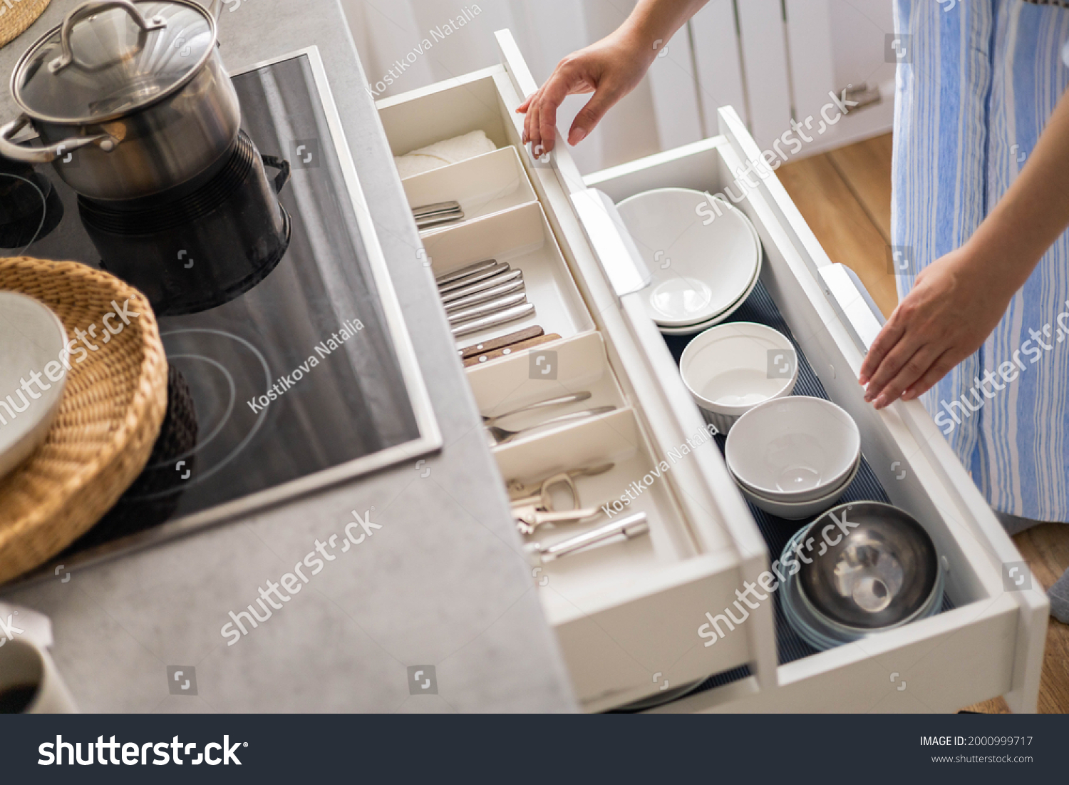 Top view modern housewife tidying up kitchen cupboard during general cleaning or tidying up. Female neatly placing dishware and cutlery in drawer of table. Storage organization Konmati method #2000999717