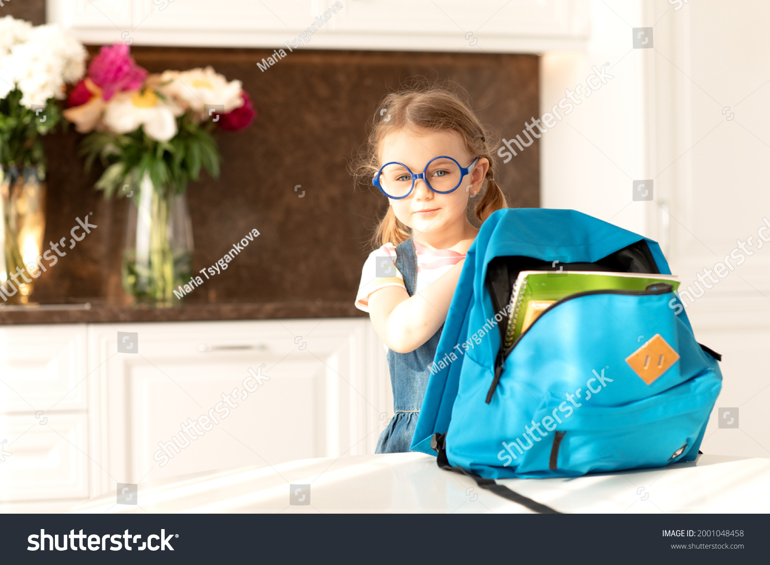 Cute child get ready for school at home sunny morning kitchen.Schoolgirl holds backpack for school day.Education,learning.Back to school.End of epidemic Coronavirus.Hello autumn #2001048458