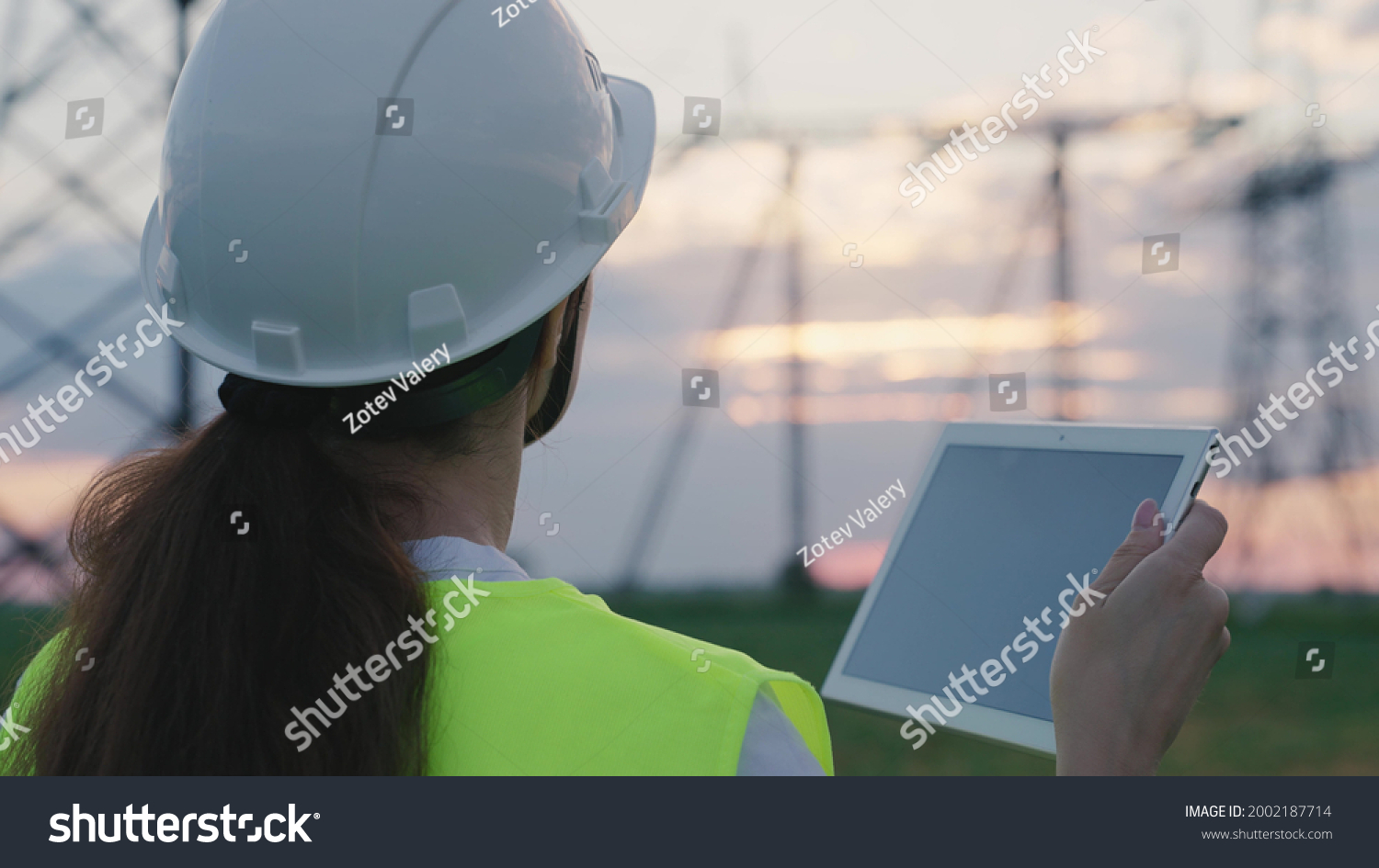 An adult woman electrician is working with a tablet on modern technologies next to a power plant, setting up energized stations through satellite control of networks, volt-installed towers, a gadget #2002187714