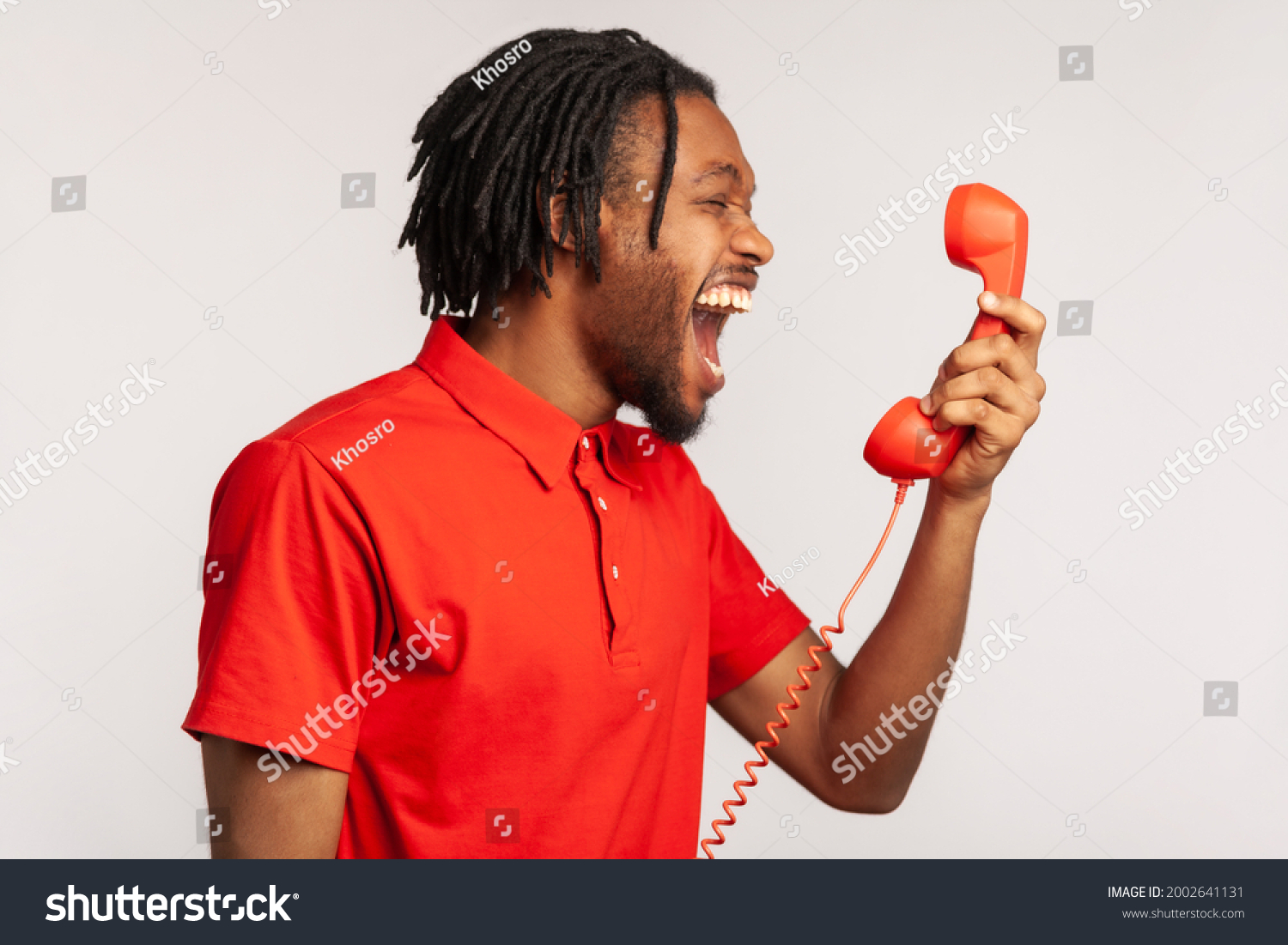 Profile portrait of male wearing red casual style T-shirt, screaming and yelling talking retro landline phone, complaining on connection quality. Indoor studio shot isolated on gray background. #2002641131