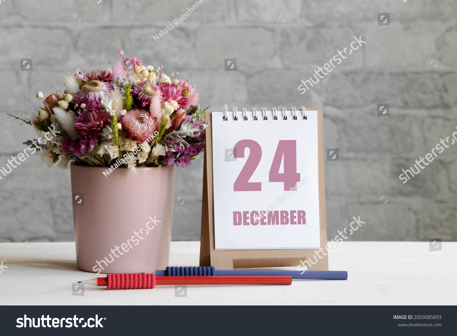 december 24. 24-th day of the month, calendar date.A delicate bouquet of flowers in a pink vase, two pencils and a calendar with a date for the day on a wooden surface.. #2003085893