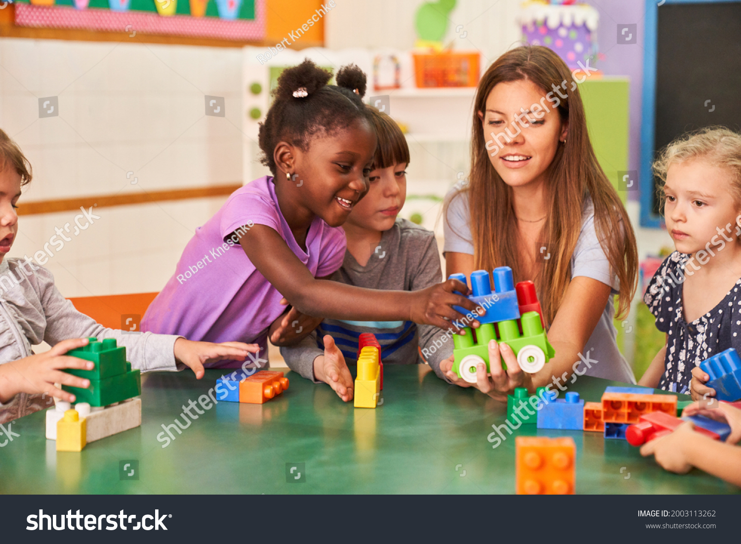 Children play together with building blocks in the international kindergarten with a kindergarten teacher #2003113262