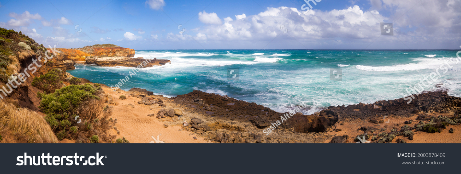 The Australian rocky coast is about 12 apostles. Strong winds drive ocean waves to the shore cliffs. A wide panorama. Sand dunes and cliffs. Blue sky with clouds on the horizon. #2003878409