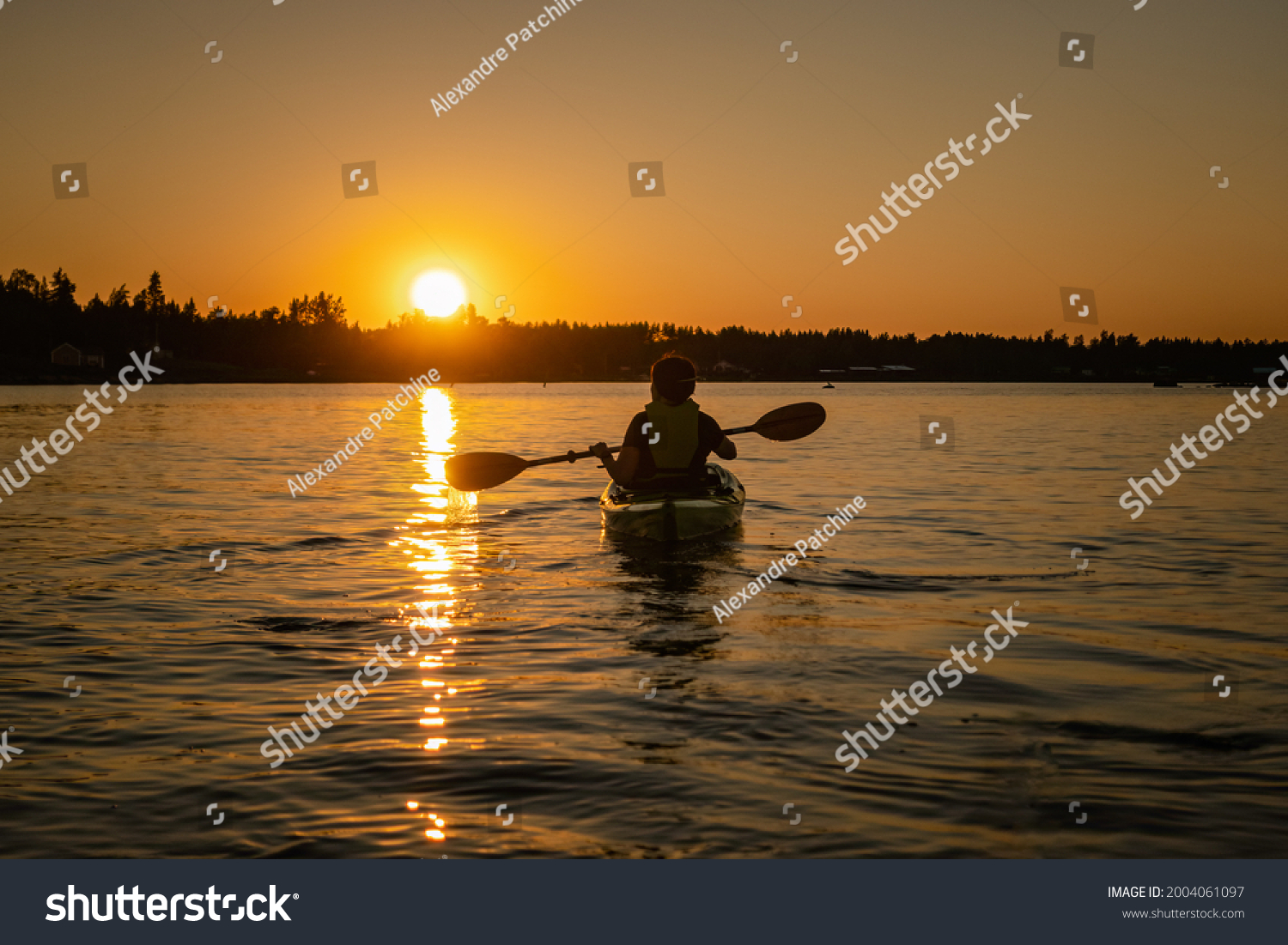 Girl kayaking and taking pause calm sea at midnight in Northern Sweden during light Summer nights. All day around Sun in polar regions. #2004061097