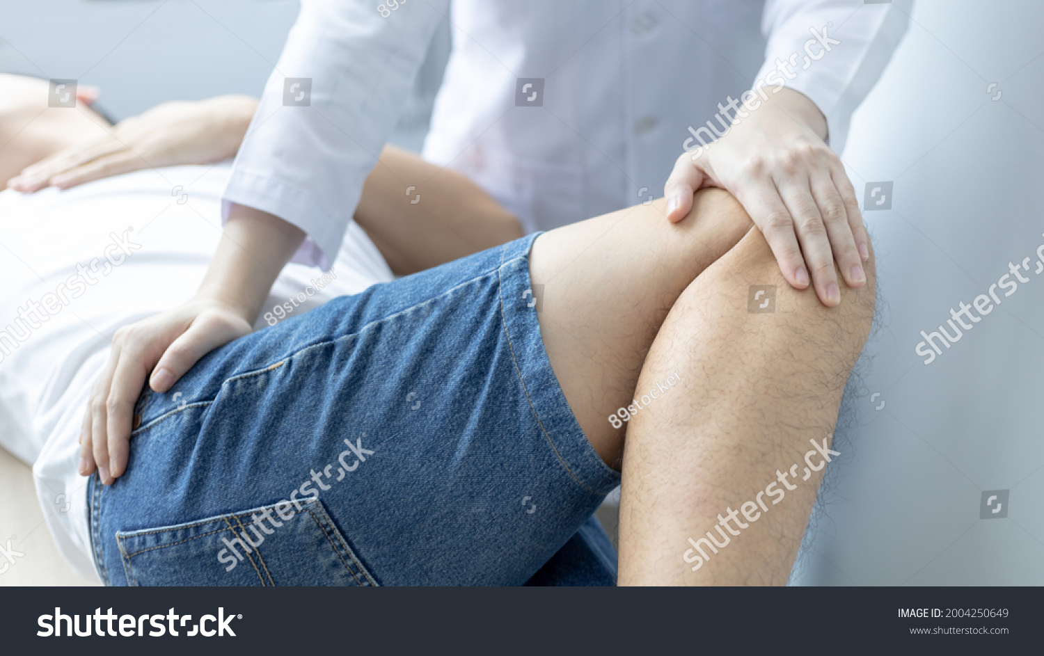 Physical therapy, Female physiotherapist treats legs and hips pain for a male patient attending in clinic, Bone arrangement, Non-surgical medical treatment, Modern medical techniques. #2004250649