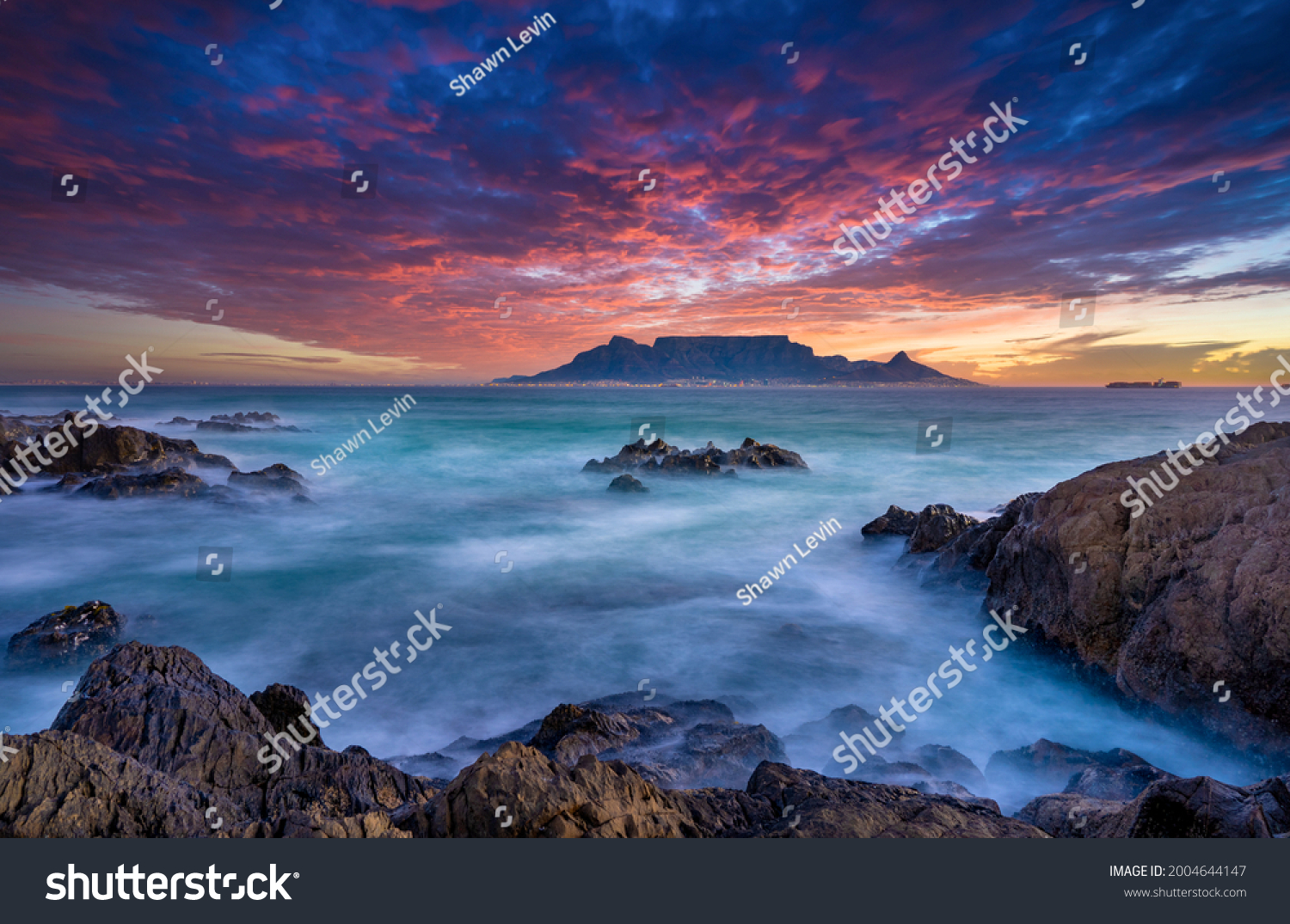 Beautiful sunset sky above a wispy long-exposure sea. Table Mountain sets the backdrop for a vibrant and colourful panorama #2004644147