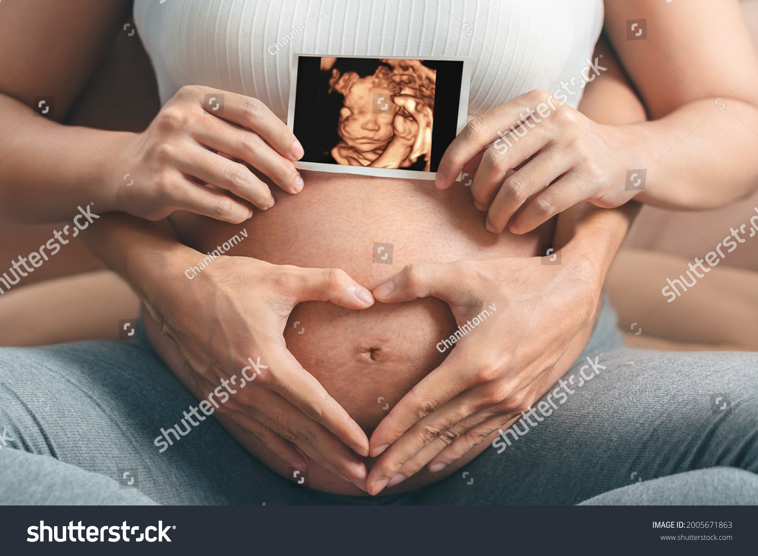 Asian pregnant woman and husband  holding hand together, holding ultrasound 4d scan image and making hand heart gesture on her belly,  Expectation of child and woman pregnancy concept. #2005671863