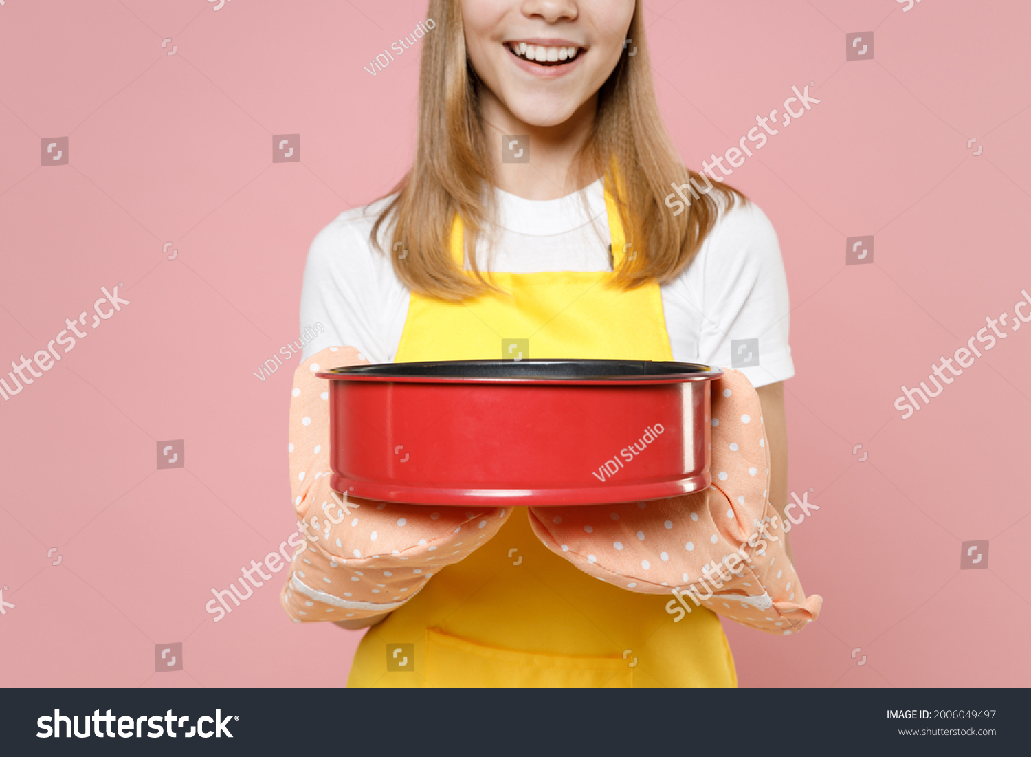 Close up cropped photo shot teen girl chef cook confectioner baker housewife in yellow apron t-shirt cap kitchen mitten potholder hold metal baking pie form isolated on pink background. Food concept #2006049497