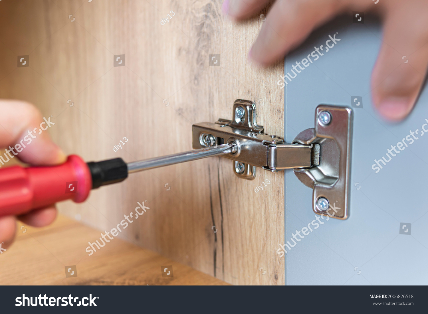 Concept of home repairing. A hand of a furniture assembler adjusting a mechanism for opening the door of the office table with a screwdriver. Close up. Self-assembly of furniture. #2006826518