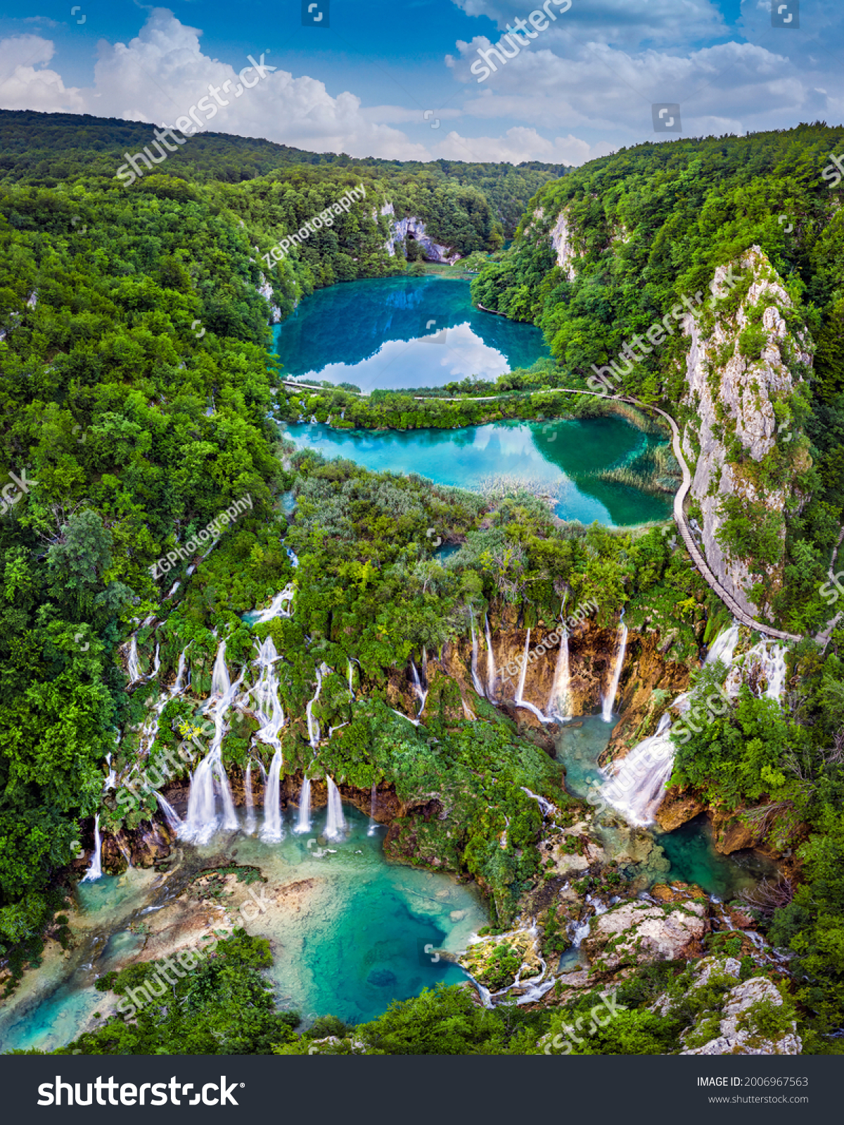 Plitvice, Croatia - Panoramic view of the beautiful waterfalls of Plitvice Lakes in Plitvice National Park on a bright summer day with blue sky and clouds and green foliage and turquoise water #2006967563