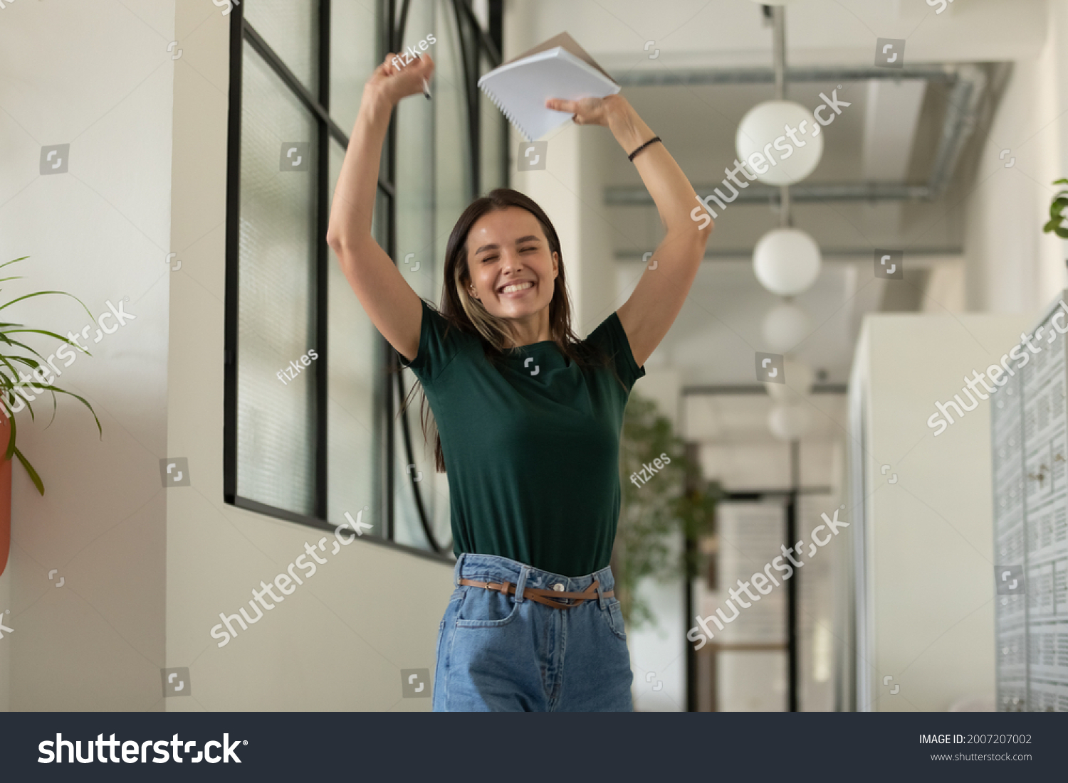 Happy excited student celebrating success, passed exam, high test grade, good result. Millennial girl feeling joy, dancing in office corridor. Candidate getting hired after successful job interview #2007207002