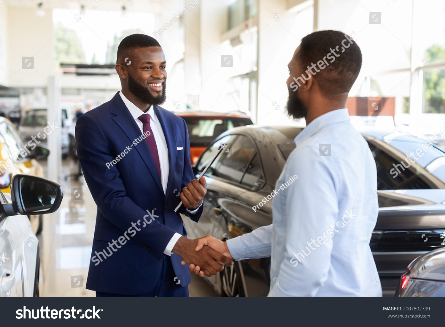 Smiling Car Seller Shaking Hands With Client After Successful Deal, Happy African American Man Buying New Vehicle In Dealership Center, Making Agreement With Salesperson In Modern Auto Showroom #2007802799