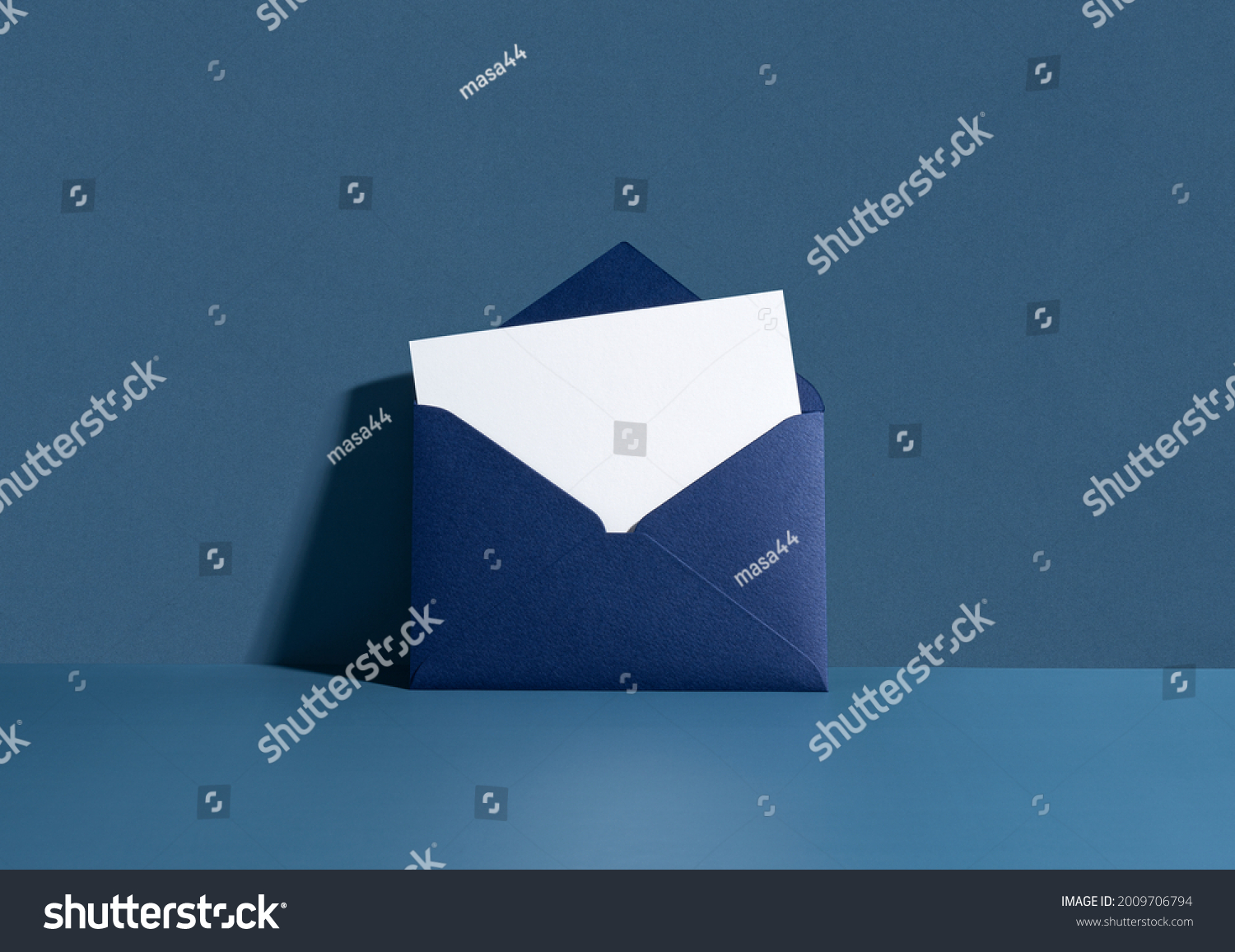 White card in a dark blue seal leaning against a blue wall. Invitation mockup, long shadow. #2009706794