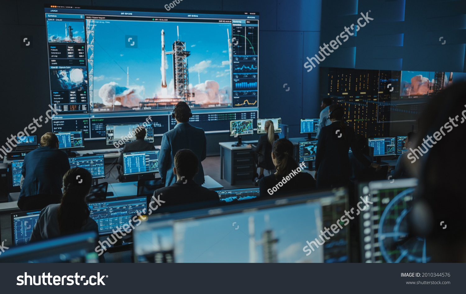 Group of People in Mission Control Center Witness Successful Space Rocket Launch. Flight Control Employees Sit in Front Computer Displays and Monitor the Crewed Mission. Team Stand Up and Watch. #2010344576