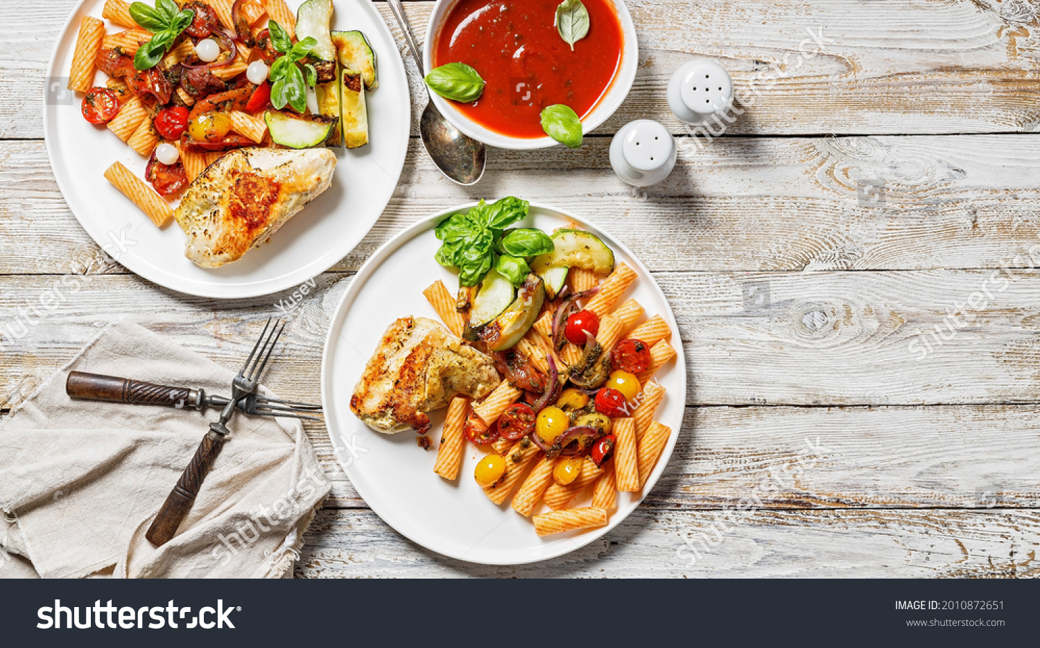 Food banner. Grilled turkey fillet, penne pasta with tomatoes, spices, Parmesan cheese and fresh basil. Tomato sauce. Traditional Italian cuisine. Two servings on a wooden background. Copy space #2010872651
