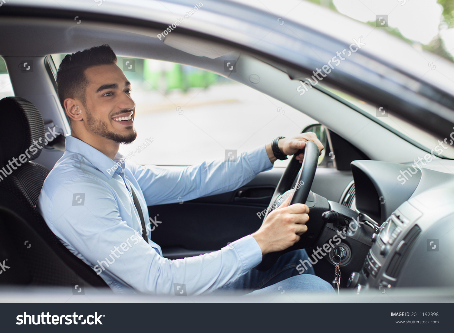 Excited arab guy going to office in the morning, driving his car, side view, copy space. Cheerful middle-eastern young man looking at the road, sitting inside luxury automobile, going home from job #2011192898